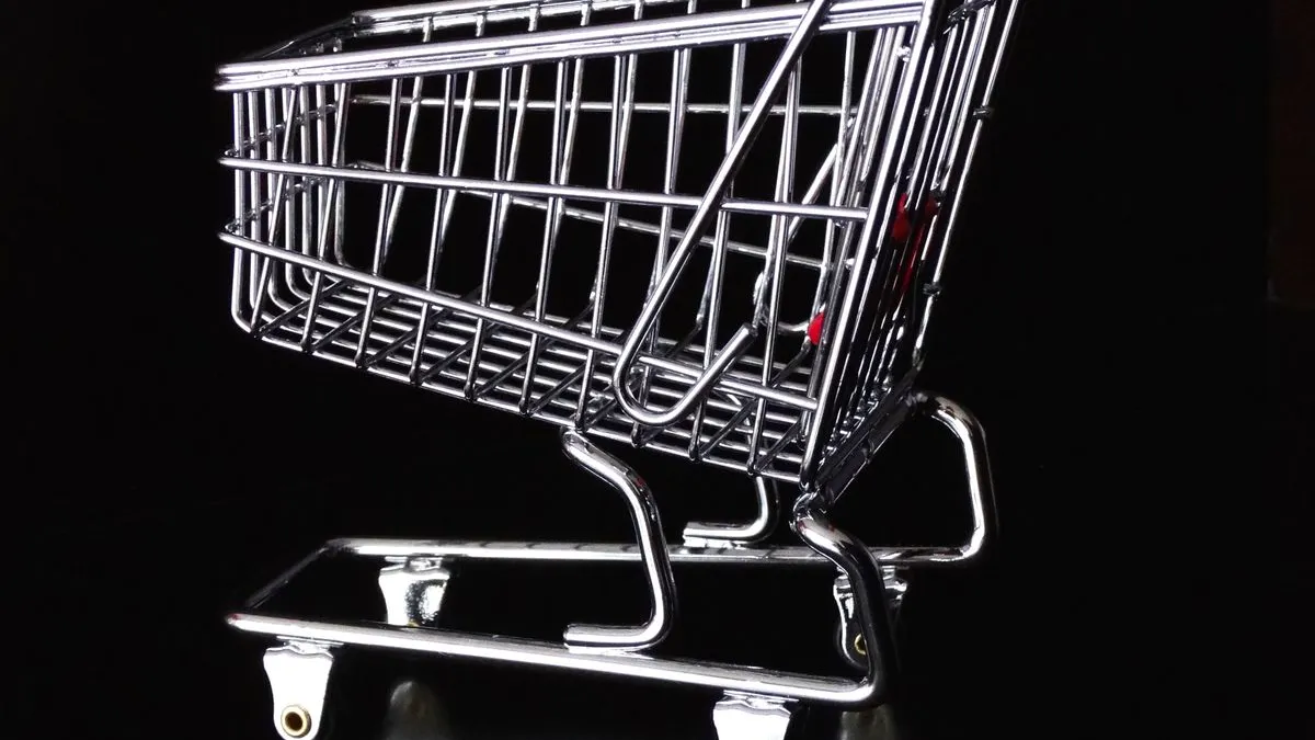 Carrito de la compra metálico en miniatura, vacío, sobre un fondo negro con iluminación dramática.
